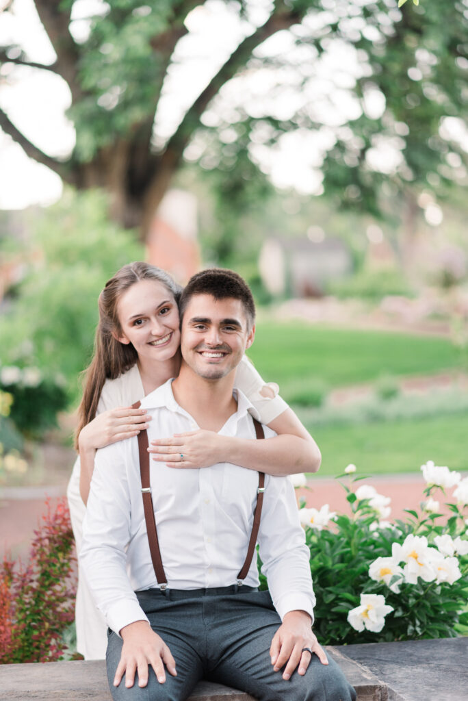 A sweet couple poses for their Colorado springs engagement photos near white flowers in a garden popular for 