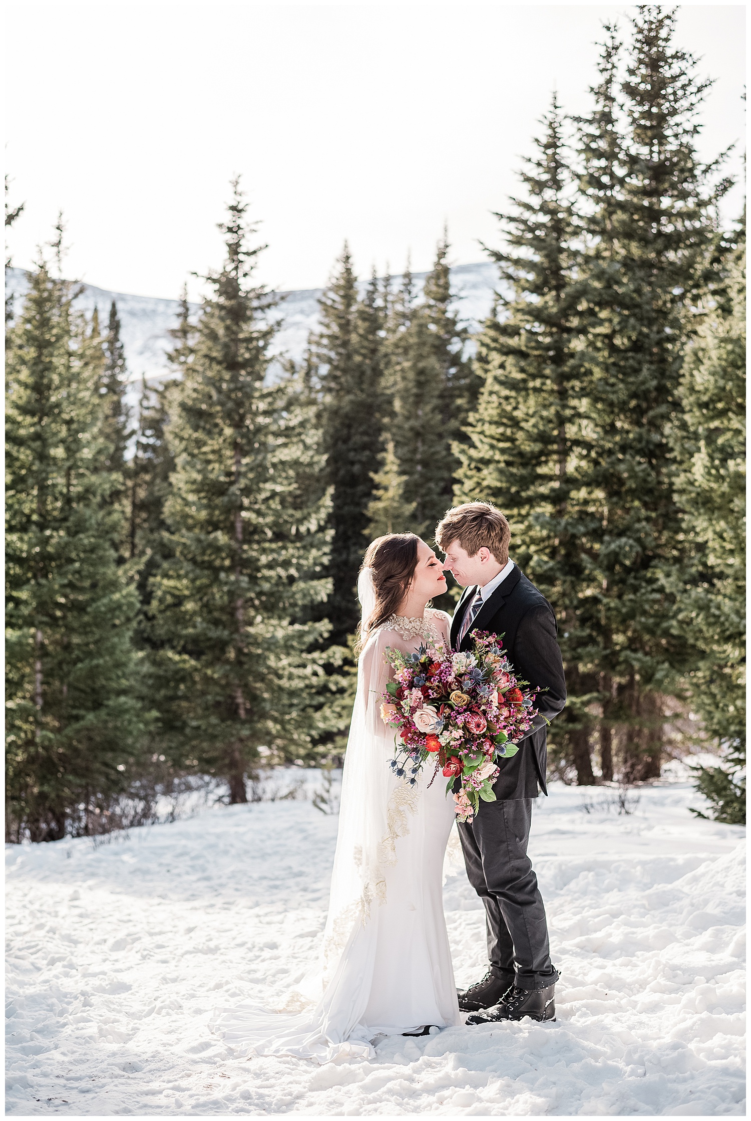 Bride and groom facing each other touching noses on a snow covered mountain top in the best month to get married in Colorado