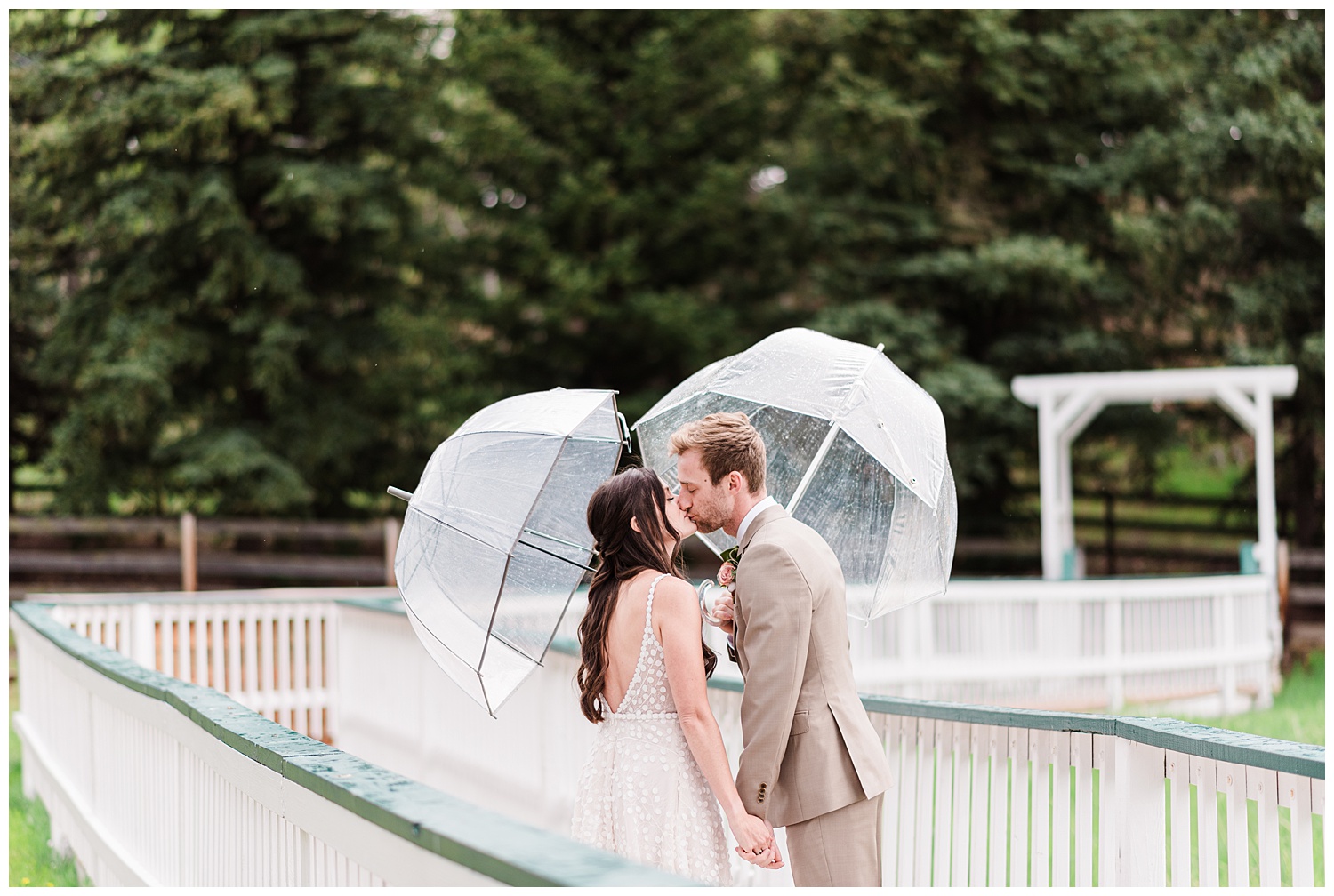 Bride and groom share a kiss on a bride while they both hold umbrellas in the best month to get married in Colorado 