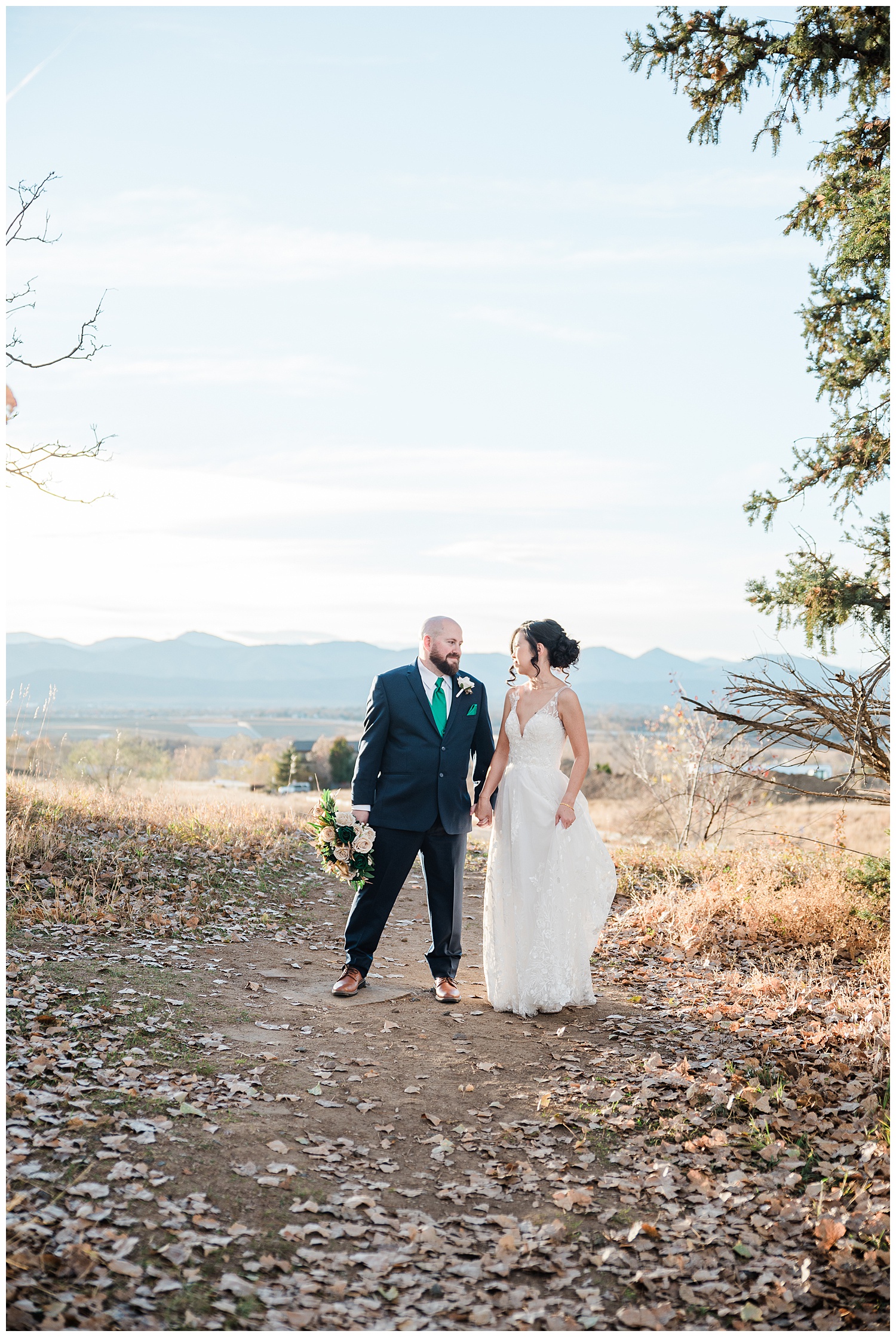 Bride and groom stand in front of a mountain view holding hands and looking towards one another with bodies toward the camera during the best month to get married in Colorado