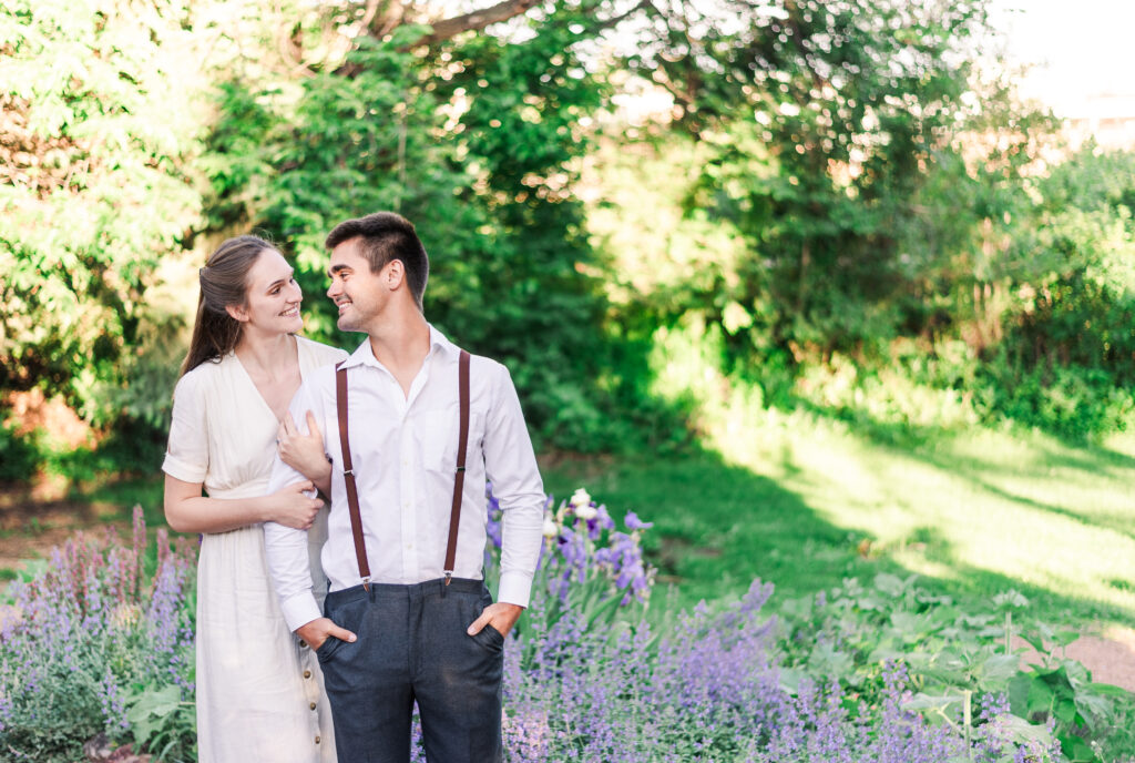 For their engagement photos, a young couple poses in front of a purple flowing bush and share a sweet look for Microwedding Denver Wedding Photographer