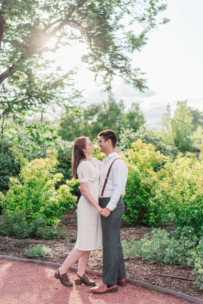 Two young people look at each other and hold hands in front of a glowy bush for Denver wedding photographer