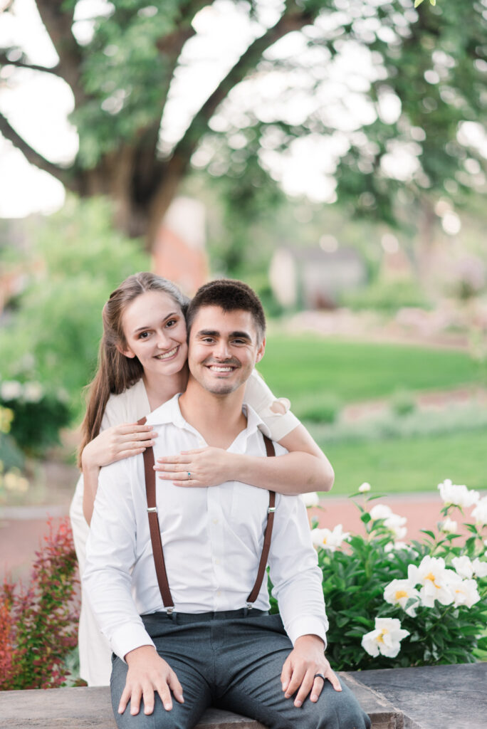 A sweet couple poses near white flowers in a garden popular for Colorado wedding photographers