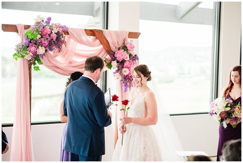 bride and groom hold a single rose during their wedding ceremony inside The Oaks