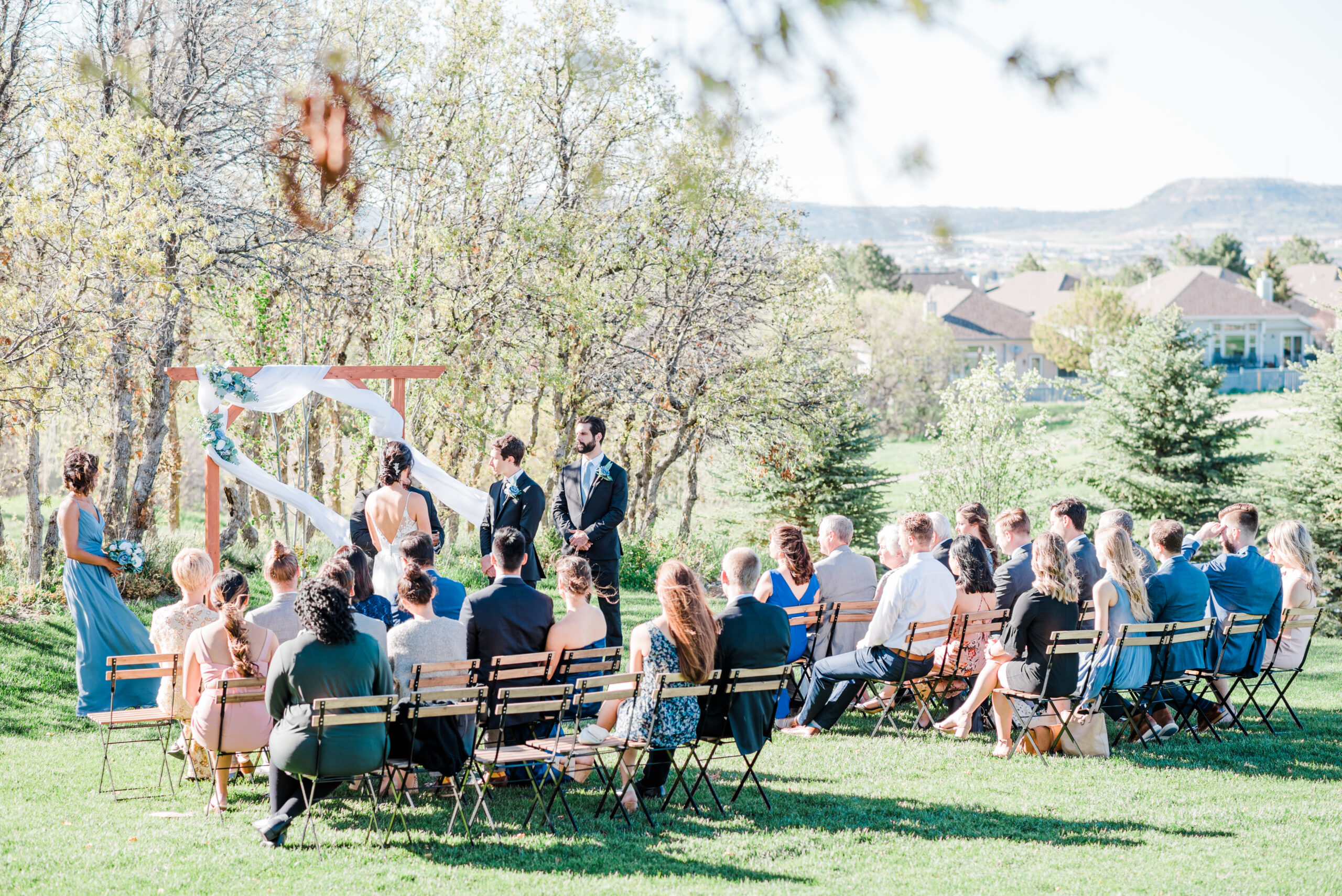 Guests sit and watch an outdoor ceremony at The Oaks along the scrub trees while bride and groom exchange vows