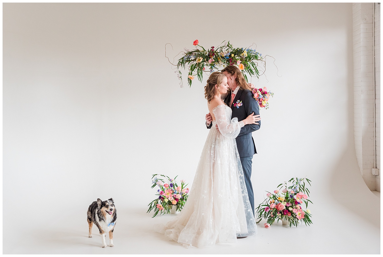 Bride and groom inside Realm Denver embrace in front of the Open Space area as their alter with their dog patiently standing watch nearby.