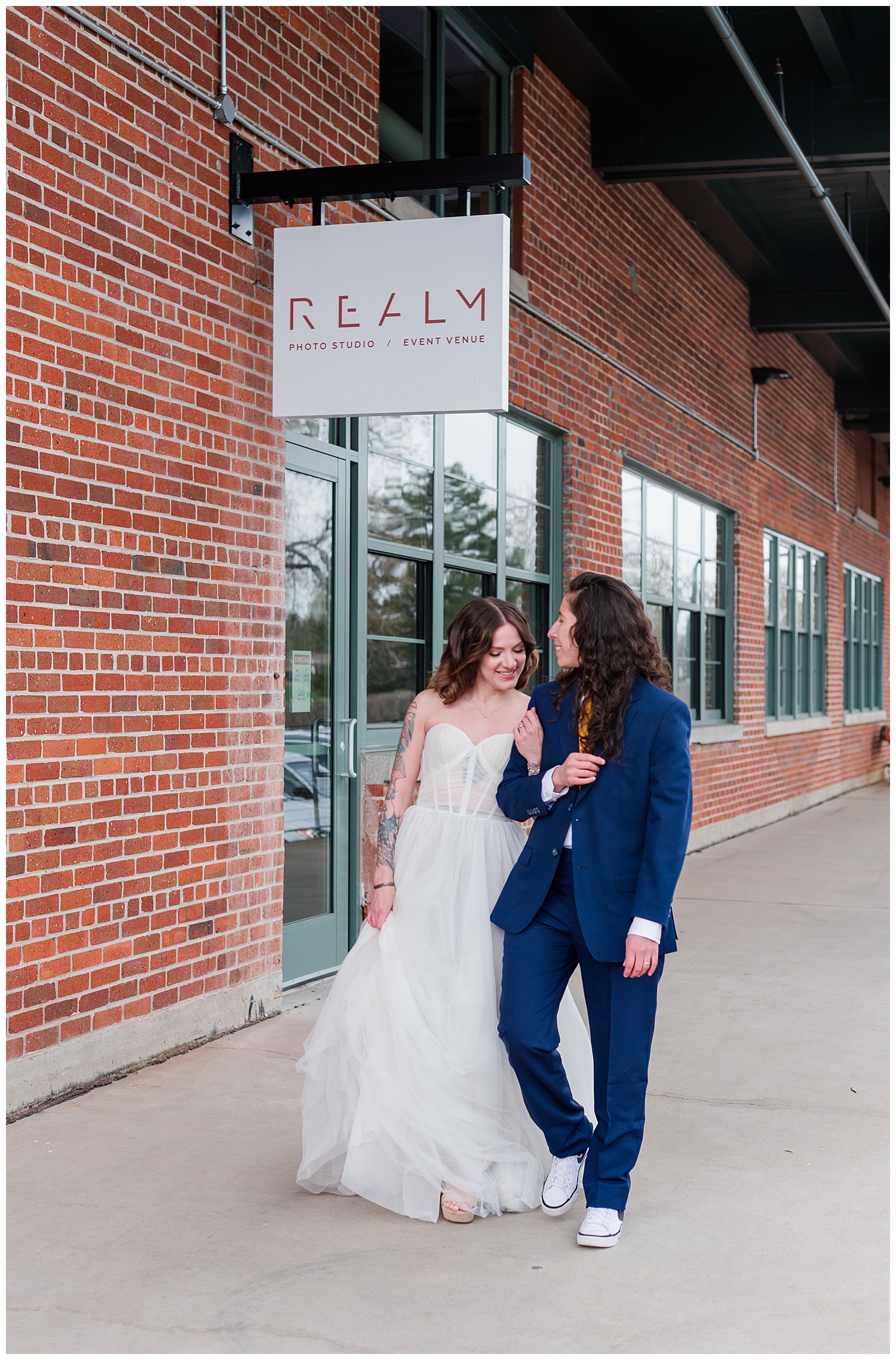 A couple walks along the sidewalk at Realm Denver arm in arm in wedding attire