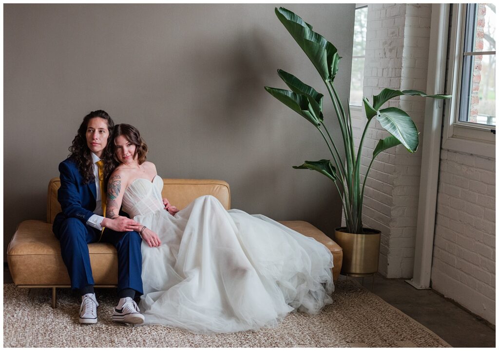 A couple cuddles on a light brown leather couch in wedding attire insde the Open Space of Realm Denver, one of the wedding venues in Denver