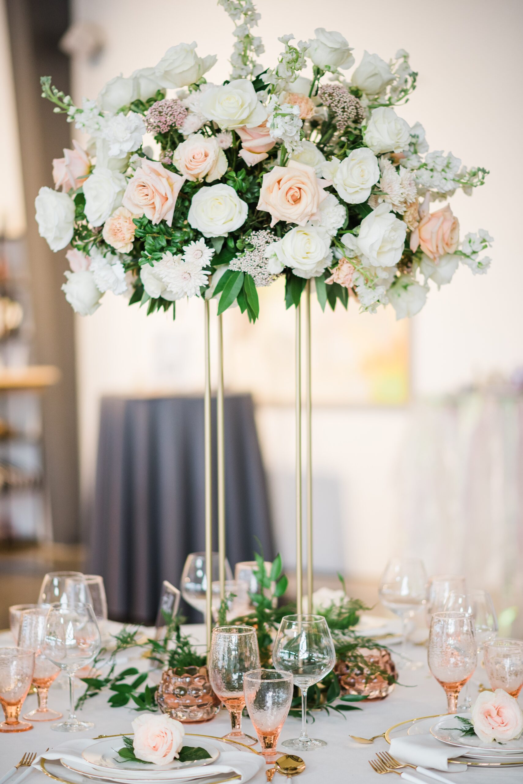 A shot of a reception table with tableware and a tall centerpiece holding a bouquet of pink and white roses