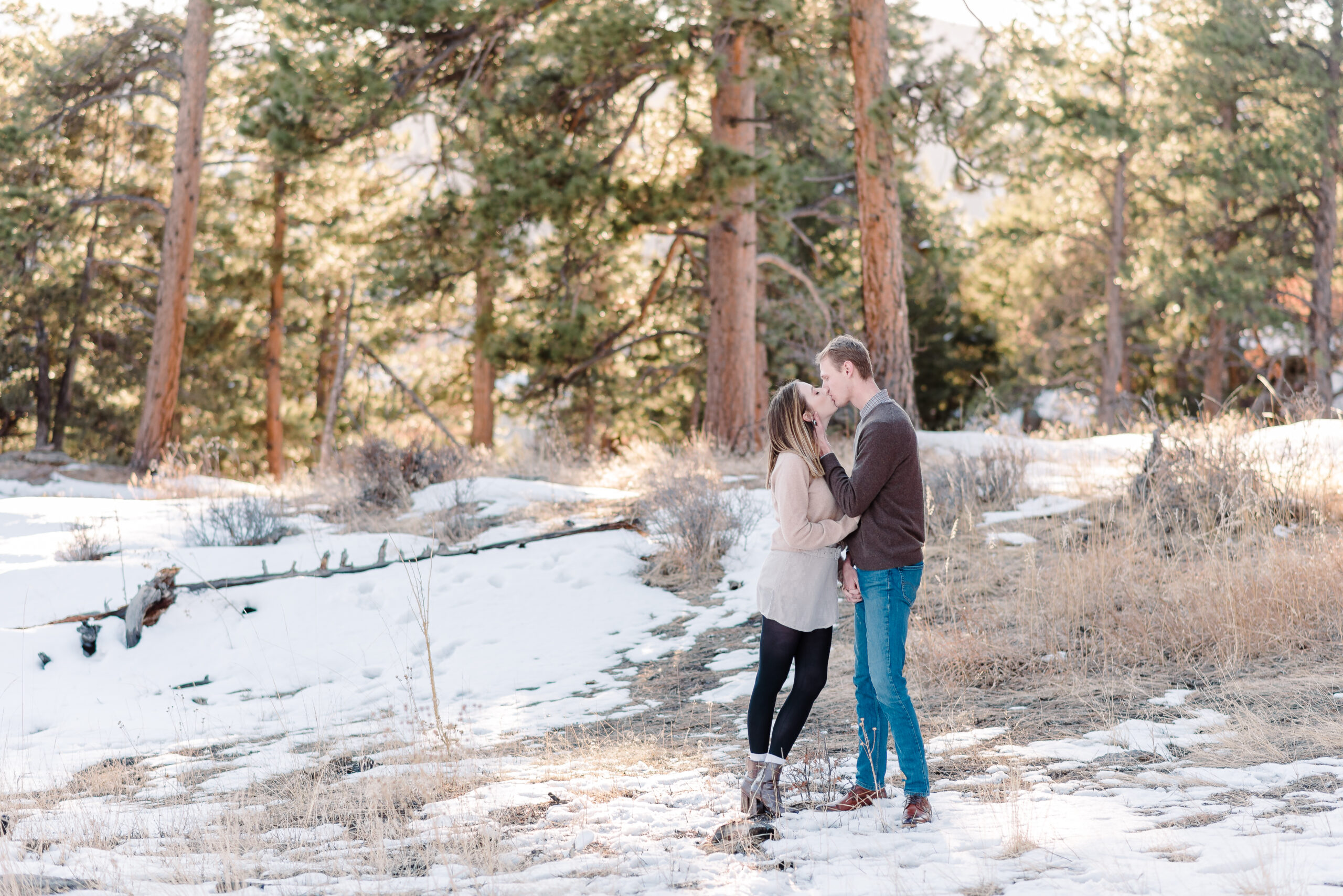 A man and woman face each other and embrace while kissing in the wooded area of Mt Falcon with snow covering the ground